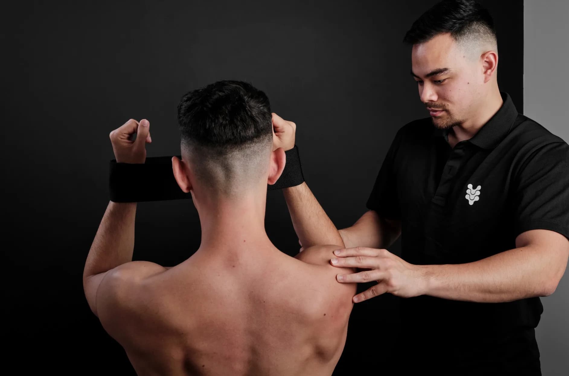 A physiotherapist at The Spinal Studio assessing a client's shoulder as he lifts a band overhead